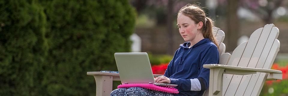 Student in chair outside on laptop